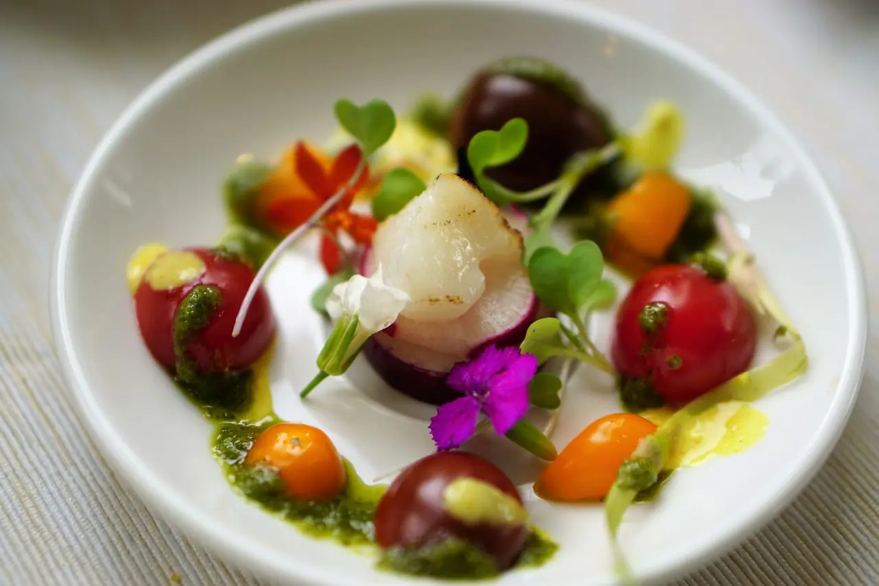 A restaurant plate of seared scallop and heirloom tomatoes finished with microgreens